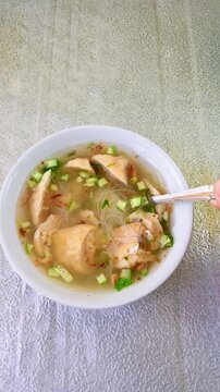 Person holding a spoon eating traditional Indonesian food Model or Tekwan soup in bowl