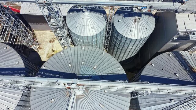 Large silos and storage tanks stand at an industrial facility. The scene shows the tops of the silos arranged in a circular pattern. Metal structures connect the storage units.