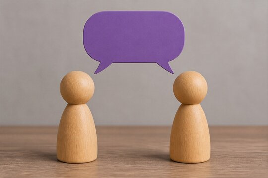 Wooden figures facing each other with purple speech bubble on tabletop