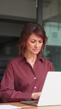 Mature latin businesswoman working on laptop in office. Focused woman banker uses pc technology to manage business finance online. Female banking manager types at corporate workplace. Vertical