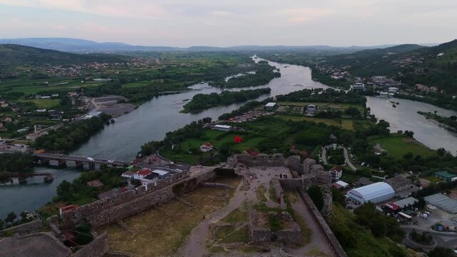 Aerial drone footage revealing Rozafa Castle above Shkoder, with its ancient stone fortifications in the foreground and the Buna and Drin river system extending through the surrounding Albanian countr