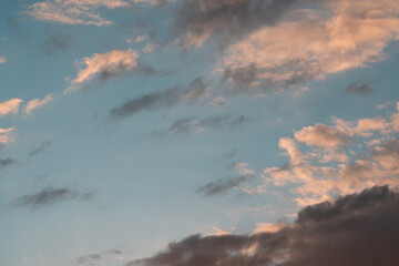 Fototapeta premium Soft blue evening sky filled with warm peach cloud bands and darker drifting layers, creating calm yet dramatic sunset atmosphere with open negative space, layered texture, and natural light