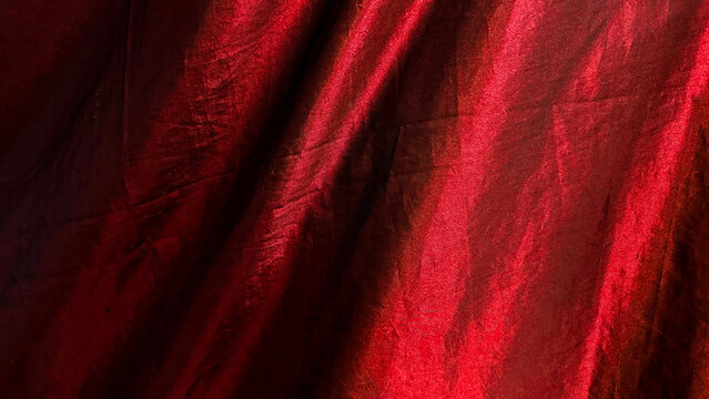 Luxury red silk satin fabric texture background. Elegant shiny crimson draped cloth with soft waves and light reflections, glossy curtain material backdrop for luxury design and fashion.