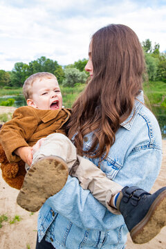 crying toddler boy held by mother during outdoor walk in park