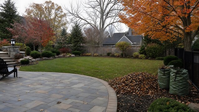 Beautifully landscaped backyard with stone patio, lawn, fall foliage trees, and leaf pile ready for collection.
