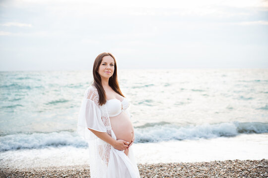 Smiling pregnant woman 35-39 year old wearing bikini over sea at beach outdoors. Looking at camera. Maternity clothes.