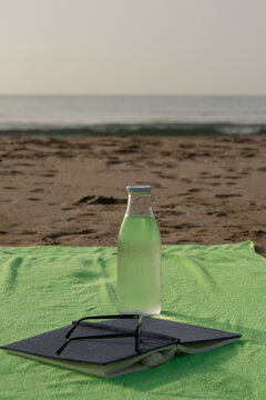 Vertical close up of beach towel with book sunglasses and water bottle