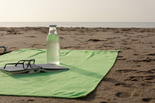 Beach towel with book sunglasses and glass water bottle by sea