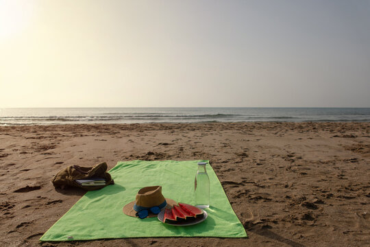 Beach towel with book watermelon and fresh water by the sea