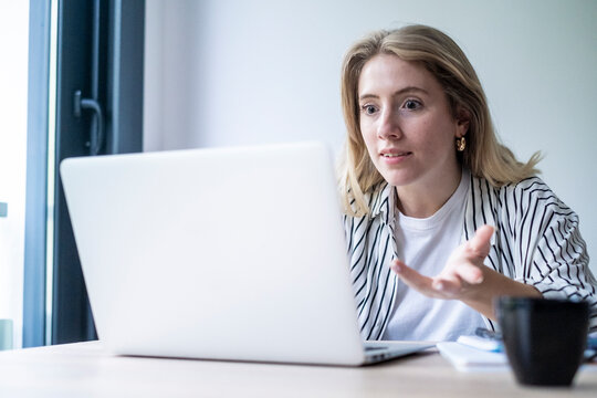 Woman facing technical issues and feeling stressed while looking at her laptop screen, communicating a sense of confusion and frustration during a remote work meeting