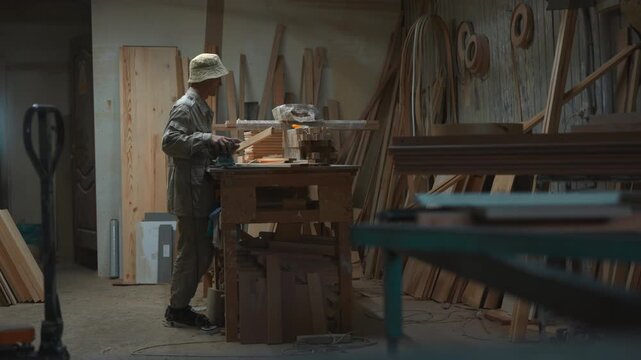 Woodworker aligning stacked lumber at cluttered workbench in dim workshop, careful carpentry process with palm sander, steady hands, sawdust, timber grain, quality check
