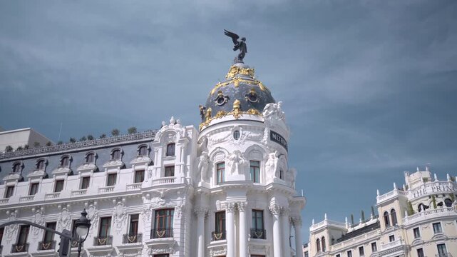 Ornate Beaux-Arts corner building with domed tower, gilded ornament, winged statue, stone facade, arched windows, and rooftop details against pale blue sky, with architecture, building, dome, statue