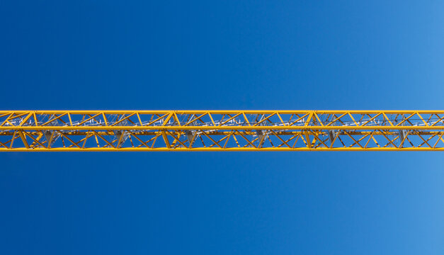 Yellow construction crane boom structure against blue sky