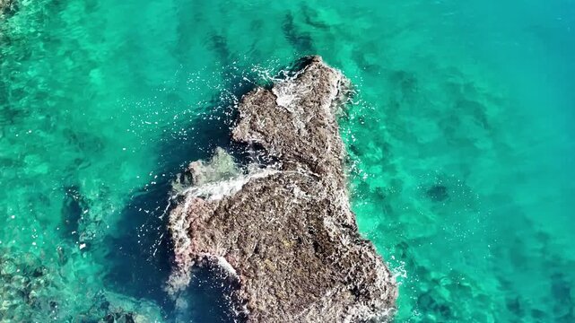 Aerial view of waves splashing against rocky outcrop surrounded by vivid turquoise antalya sea.