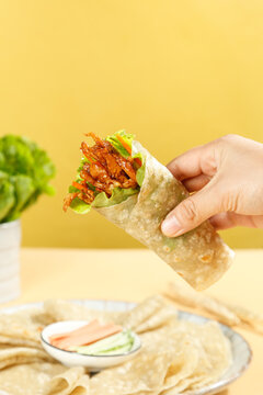 Fresh Breakfast Wrap with Bacon and Lettuce Held in Hand Against Yellow Background