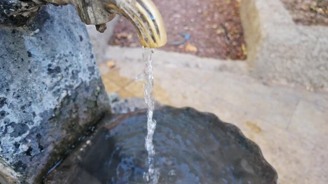 Clear water trickles from antique bronze spout into weathered stone fountain basin in antalya.