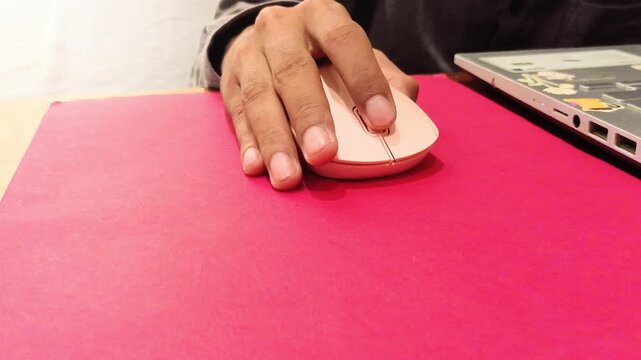 Close up of person hand using pink wireless computer mouse and laptop on desk