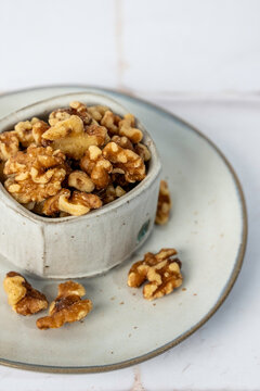 Walnuts in a ceramic bowl on a ceramic plate on a white tile surface 