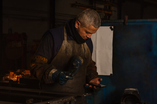 Industrial worker checking smartphone beside metal pieces prepared for welding