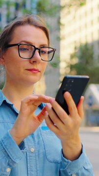 Caucasian woman in glasses walking around the city and using smartphone
