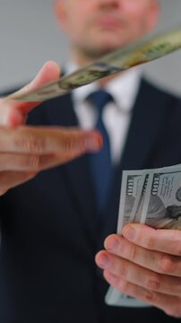 Formally dressed man carelessly throws US Dollar bills towards the camera