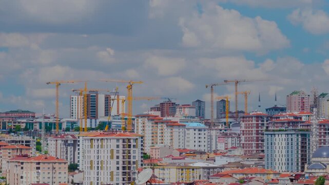Timelapse: yellow tower cranes moving above construction sites and residential apartment blocks in Istanbul, with fast clouds crossing a cloudy sky. Urban construction, development and time lapse