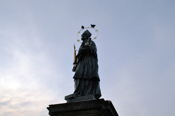 Fototapeta premium Silhouette of a saint statue with halo of stars on a pedestal against dusk sky on charles bridge in Prague for moody background and travel poster design