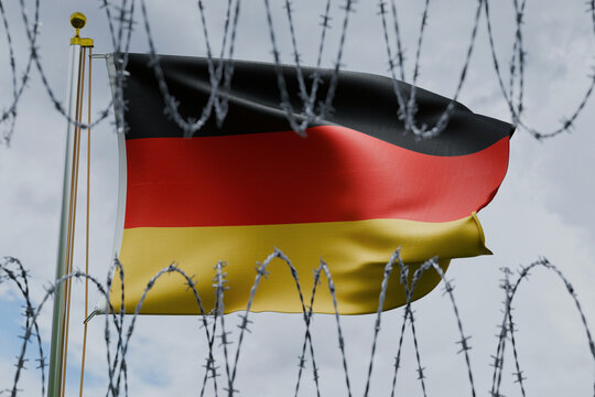 German flag waving on a flagpole, viewed behind sharp coiled barbed wire against a cloudy sky. Conceptual image representing European immigration policy, German border security, and migration control.