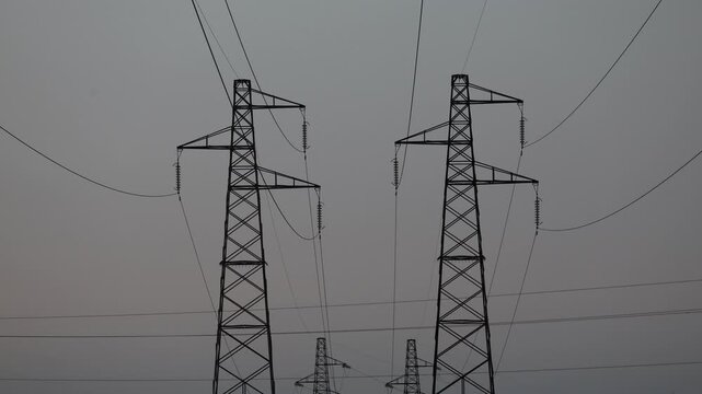 Low angle shot of two high voltage power pylons and electrical cables against a clear sky.