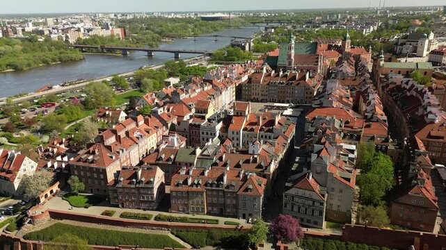 Drone footage of Warsaw Old Town with red rooftops, historic streets, colorful buildings, churches and restored European architecture in sunny weather.