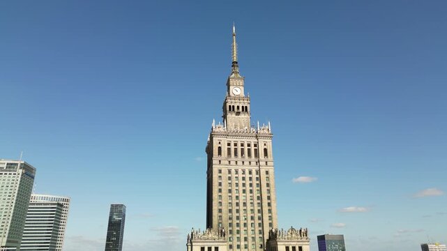 Drone footage of the Palace of Culture and Science in Warsaw, showing its historic tower, clock facade, surrounding streets and sunny city atmosphere