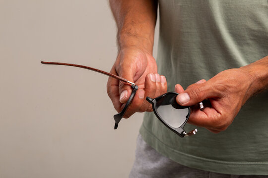 A young guy in a colored T-shirt and gray shorts holds broken glasses in his hands after unsuccessfully transporting luggage at the airport. The glasses are made of low-quality material