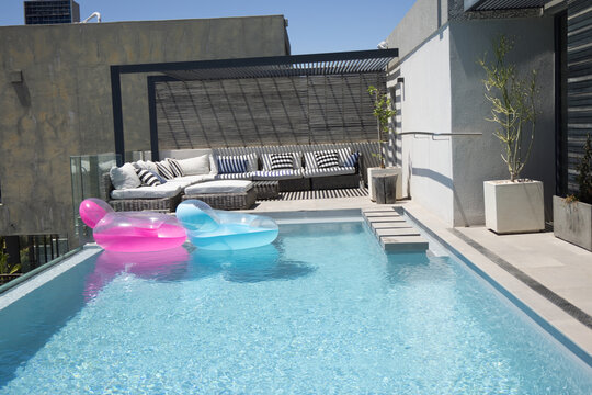 Rooftop pool centering frame, pink and blue loungers floating near left, woven sofa under pergola