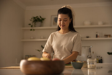 Asian woman wearing striped top preparing food on cutting board in home kitchen with wooden bowl © wavebreak3
