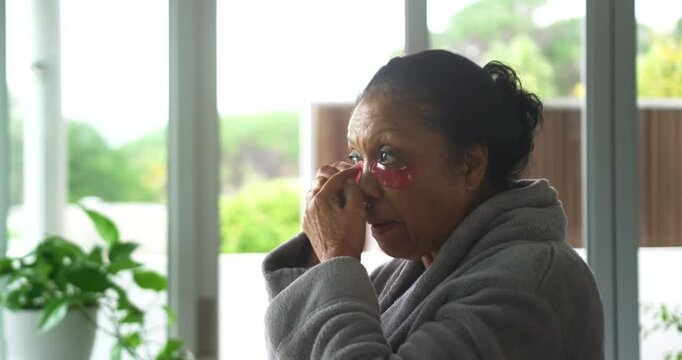 Senior African American woman with red under-eye patches pressing, adjusting in gray robe by doors