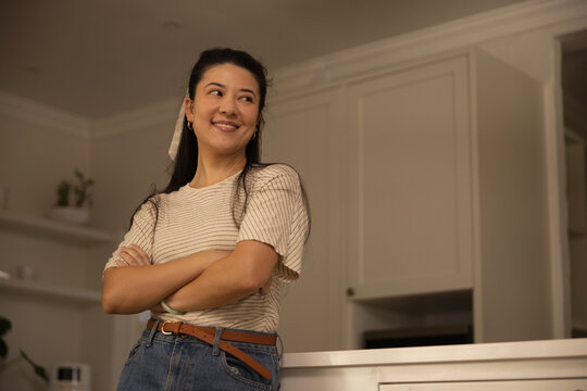 African American or Asian woman in striped shirt leaning on kitchen counter, smiling, looking right