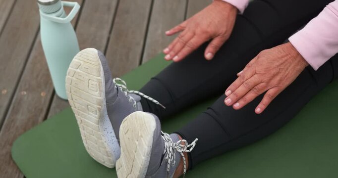 Senior female starting legs extended, leaning forward on green mat on deck, stretching to sneakers
