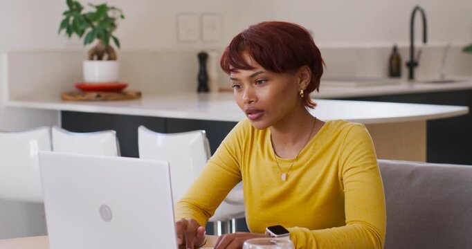 African American woman placing hands on laptop, typing and frowning while working at kitchen table