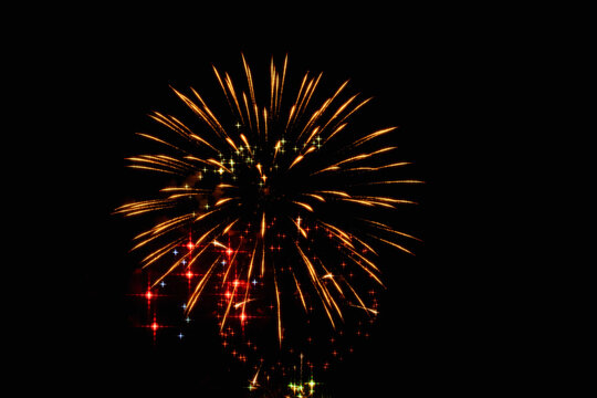 Bright golden fireworks with red accents explode against a deep black sky during a colorful nighttime celebration.