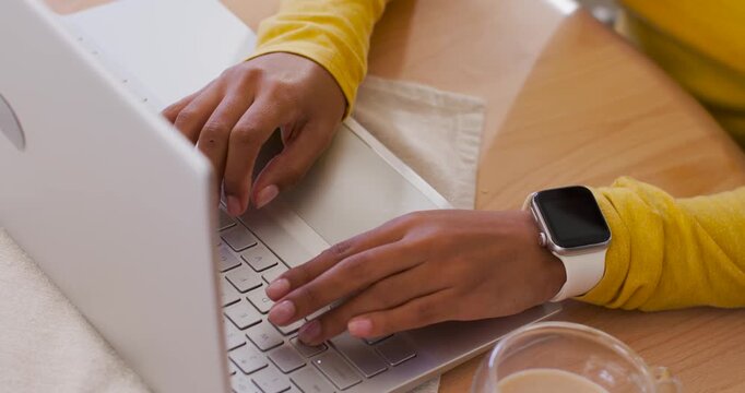African woman resting hands then starting typing on silver laptop at table, working, smartwatch