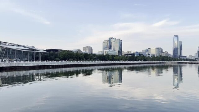 Modern panorama of the Baku embankment on the shore of the Caspian Sea in the evening. The calm water reflects the urban architecture, skyscrapers and the soft sky, creating an atmosphere of silence a