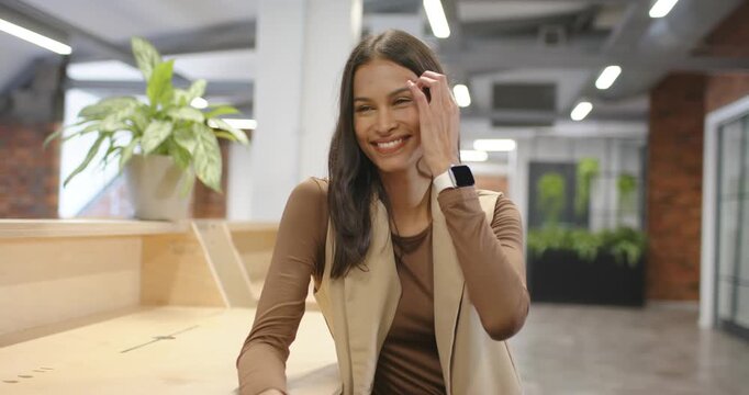African American woman sitting on bench in office, facing camera, responding, smiling, tucking hair