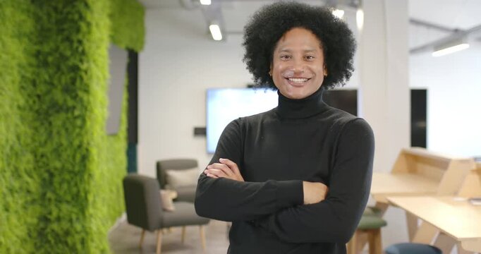 African American man arms-crossed laughing then smiling as focus tightening in office by green wall