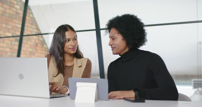 Hispanic woman and African American man at desk opening file, typing on laptop, reviewing tablet
