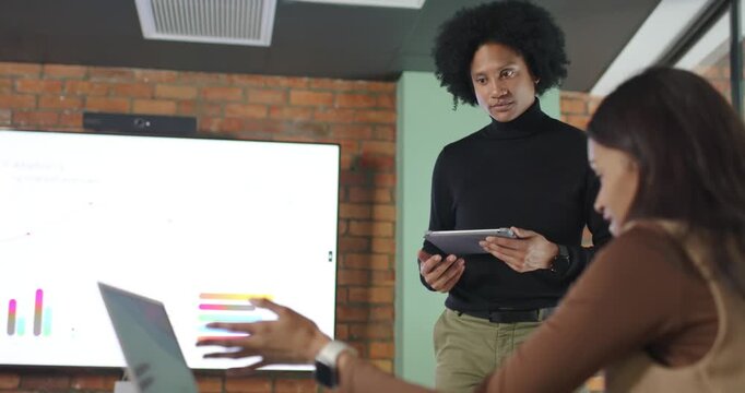 African American colleagues presenting, woman gesturing at chart display while man tapping tablet