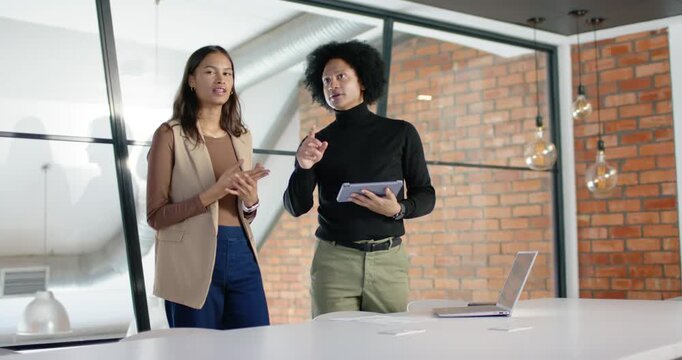 Coworkers standing behind large white table, man pointing with tablet, woman following decision