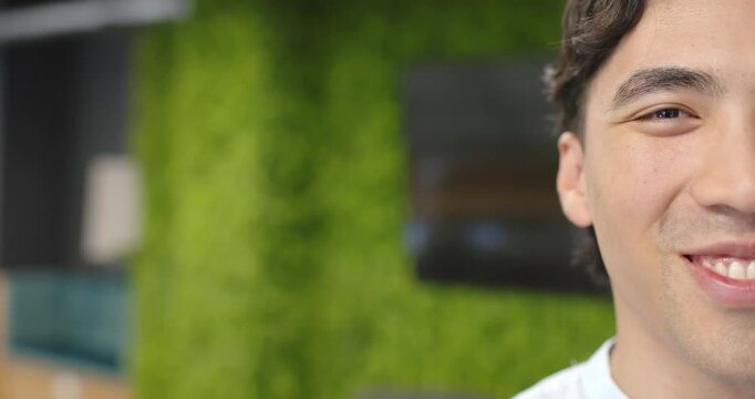 Asian male moving, camera panning right, revealing smile engaging camera by moss wall, copy space