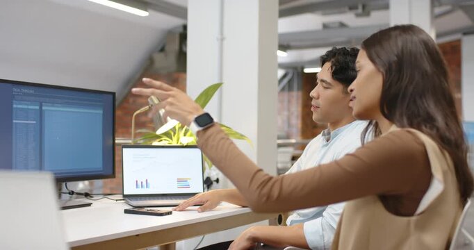 Diverse coworkers sitting at desk woman leaning pointing laptop and monitor man nodding to align