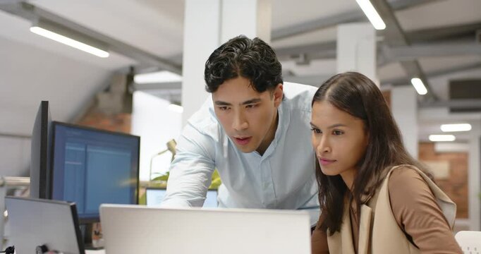 Diverse coworkers working at office desk, man coming and leaning, pointing at laptop reviewing