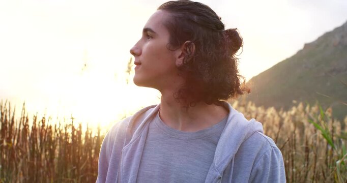 Early 20s man standing reed field in hoodie sun causing lens flare turning head scanning horizon